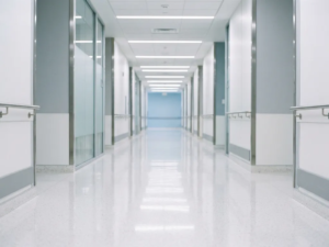 Weitläufiger Krankenhausflur mit glänzendem weißen Boden und symmetrischer Perspektive in kühlen Blau- und Weißtönen.