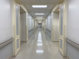 Leerer Krankenhausflur mit glänzendem Boden, weißen Wänden und Fluchtpunkt-Perspektive unter kühlem Neonlicht.