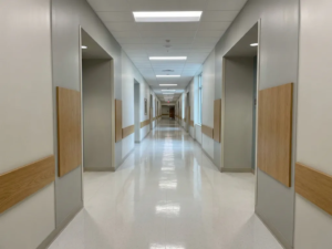 Weitläufiger Krankenhausflur mit glänzendem weißen Linoleumboden und kühler Deckenbeleuchtung, die sich zum Fluchtpunkt erstreckt.