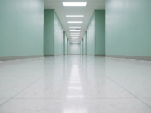 Langer, leerer Krankenhausflur mit glänzendem weißem Linoleumboden, mintgrünen Wänden und fluoreszierender Deckenbeleuchtung.