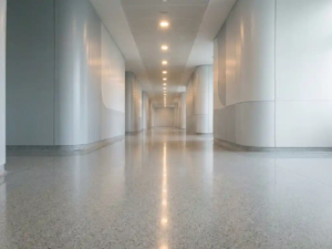 Leerer Krankenhausflur mit glänzendem weißem Boden, der Neonlicht reflektiert, und sauberen klinischen Wänden in kühlen Grautönen.