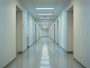 Leerer Krankenhausflur mit poliertem Linoleumboden und fluoreszierendem Licht, der in der Perspektive zu einem Fluchtpunkt führt.