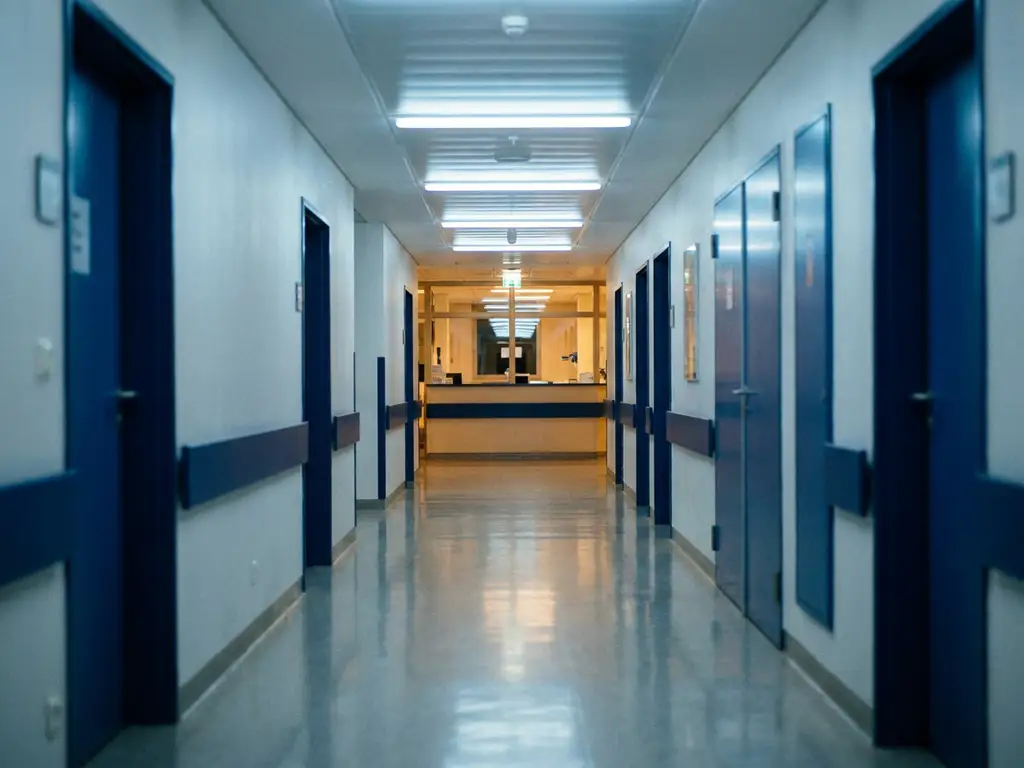 Leerer Krankenhausflur bei Nacht mit poliertem Linoleumboden, fluoreszierendem Licht und warmem Schein eines entfernten Schwesternstützpunkts.