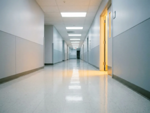 Leerer Krankenhausflur mit glänzendem weißen Boden und Fluchtpunkt-Perspektive unter fluoreszierendem Deckenlicht.