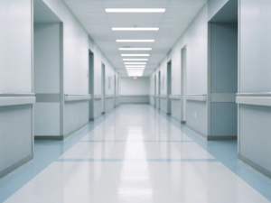 Leerer Krankenhausflur mit glänzendem weißem Linoleumboden und fluoreszierender Deckenbeleuchtung, klinische Atmosphäre in Weiß- und Grautönen.
