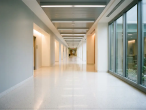 Leerer Krankenhausflur mit glänzendem weißem Boden, der Neonlicht reflektiert, und sich in die Tiefe erstreckenden klinischen Wänden.