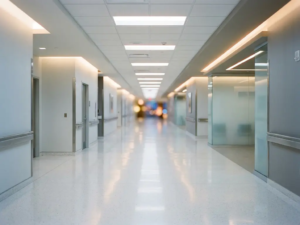 Weitläufiger Krankenhausflur mit glänzendem weißem Boden und Neonbeleuchtung, die sich in der Ferne verliert.